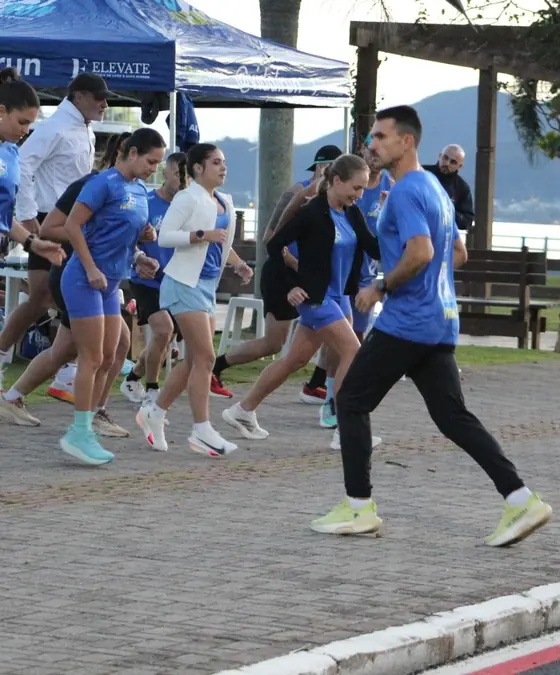 Grupo de alunos da VidalRun começando a correr juntos na orla, com o treinador à frente
